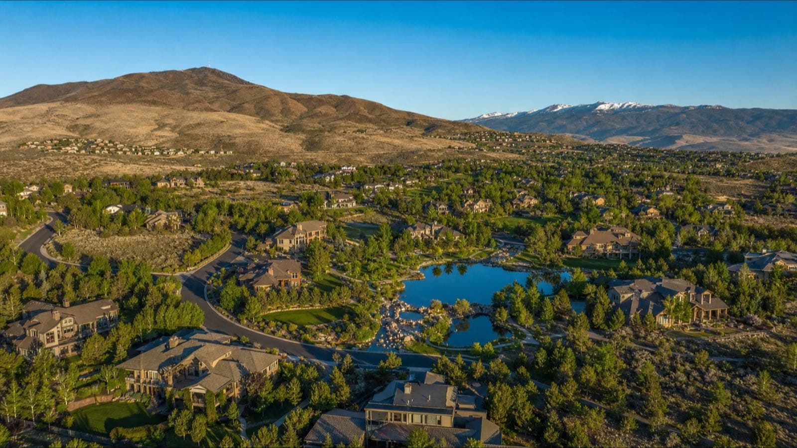 Aerial of a pond, walking paths and large homes in the Caughlin Ranch area of southwest Reno, with foothills and snow-capped peaks behind