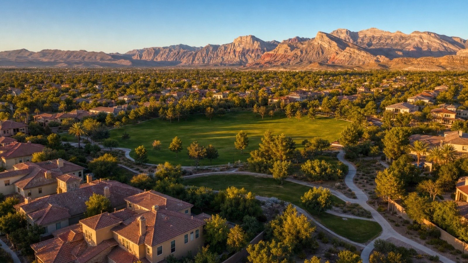 Aerial of The Trails village in Summerlin with a park lawn, paved paths and tile-roof homes below the Red Rock escarpment
