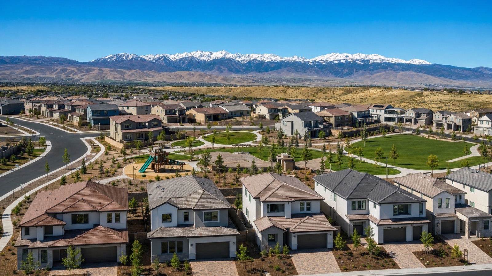 Aerial view of new production homes around a park in a south Reno, Nevada subdivision with the snow-capped Carson Range behind
