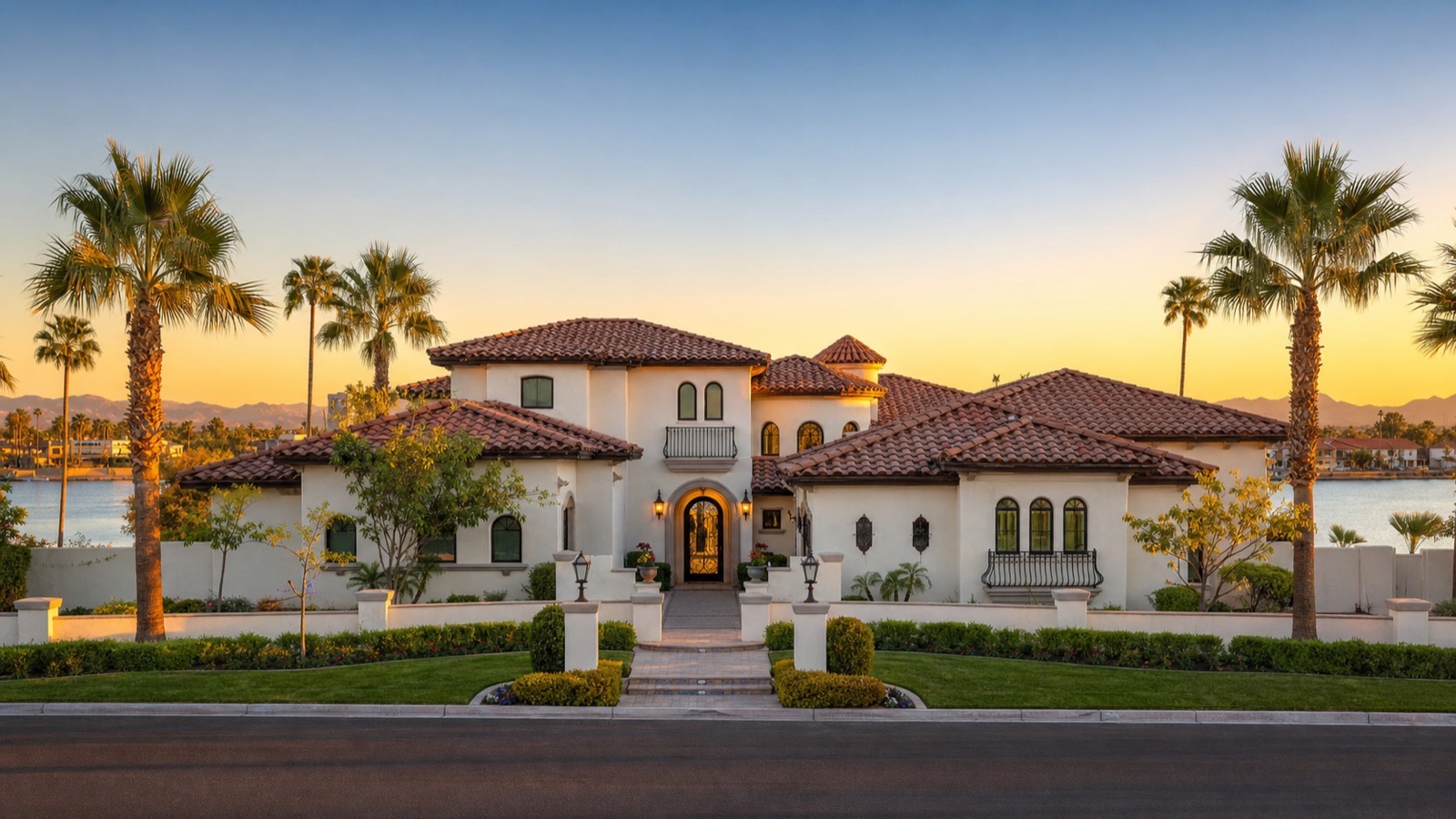 Mediterranean-style two-story lakeside home with a tile roof, palm trees and water behind it at sunset in northwest Las Vegas