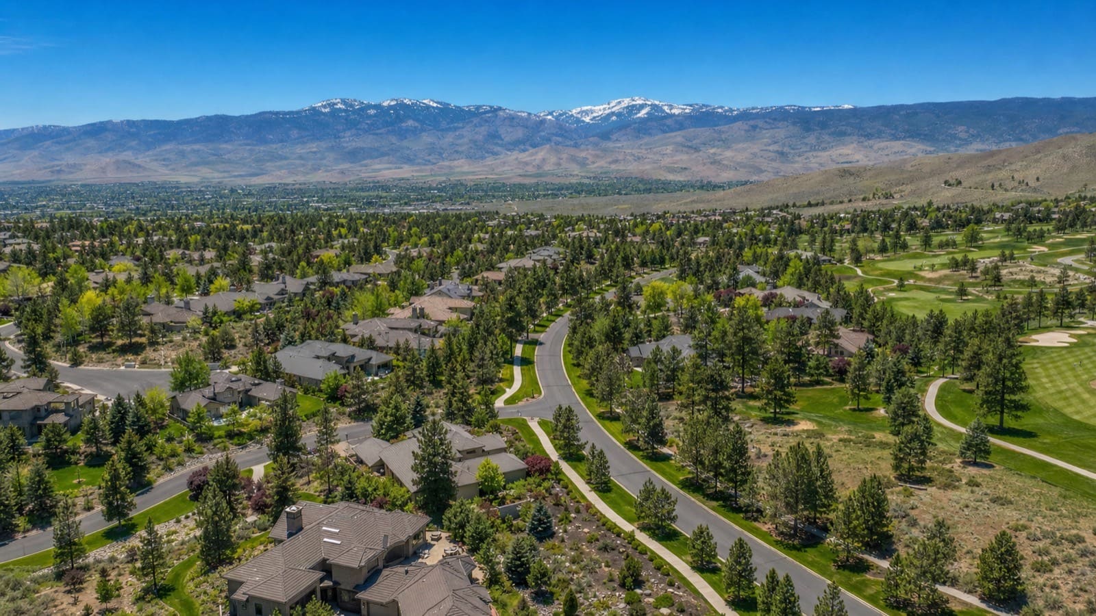 Aerial view of Caughlin Ranch homes in southwest Reno among pines and open space with the Sierra Nevada in the distance