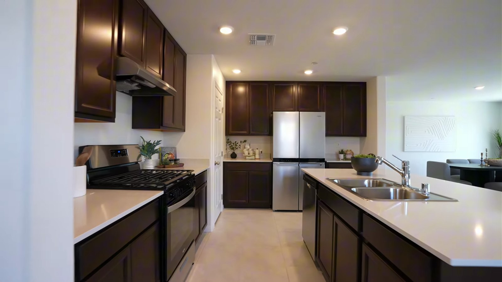 KB Home Plan 2069 model kitchen at Landings at Aven with dark cabinets, a quartz island with a double sink, a gas range and a stainless refrigerator