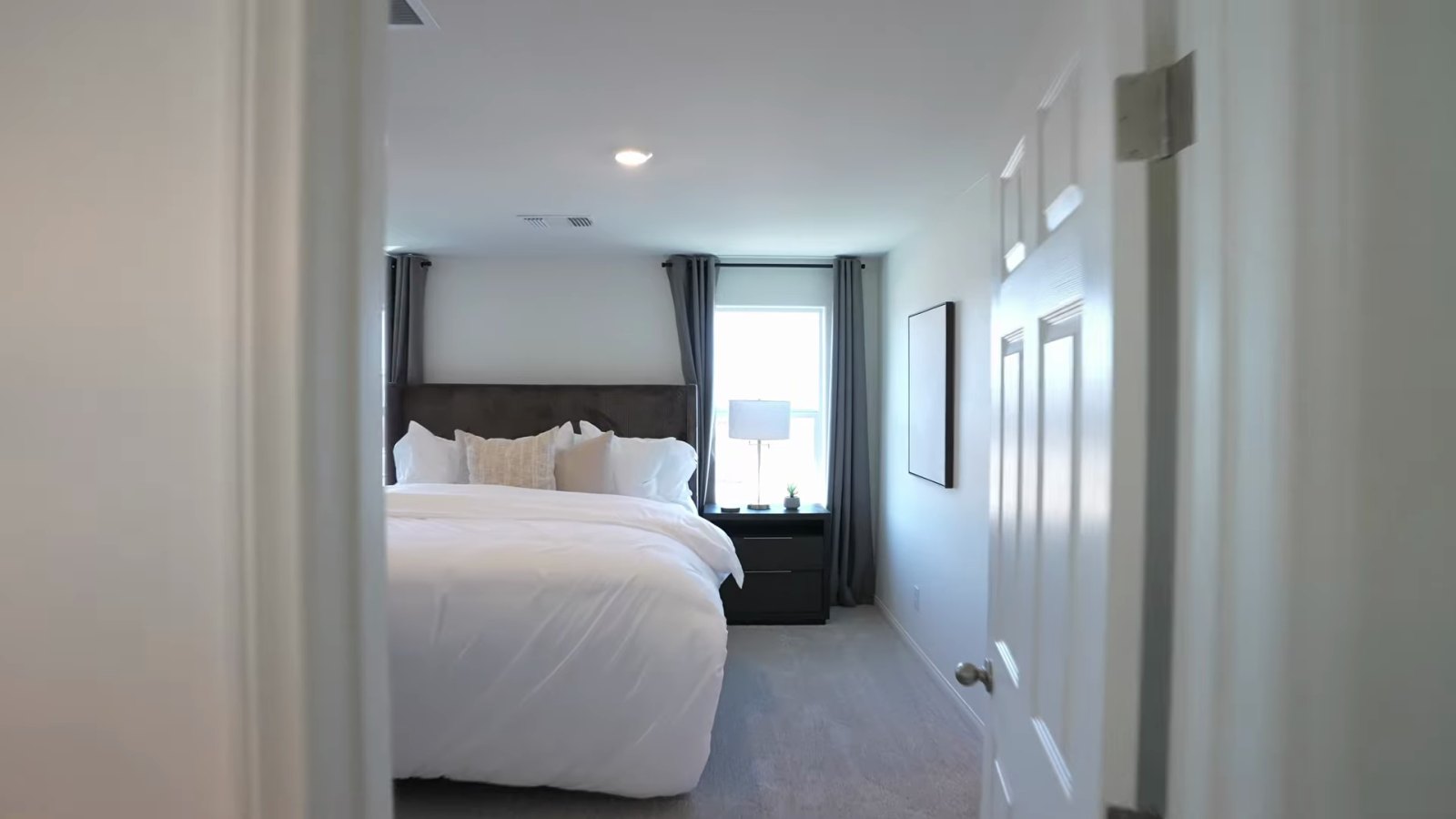 Primary bedroom in the KB Home Plan 2069 model at Landings at Aven with a king bed, nightstand and window light