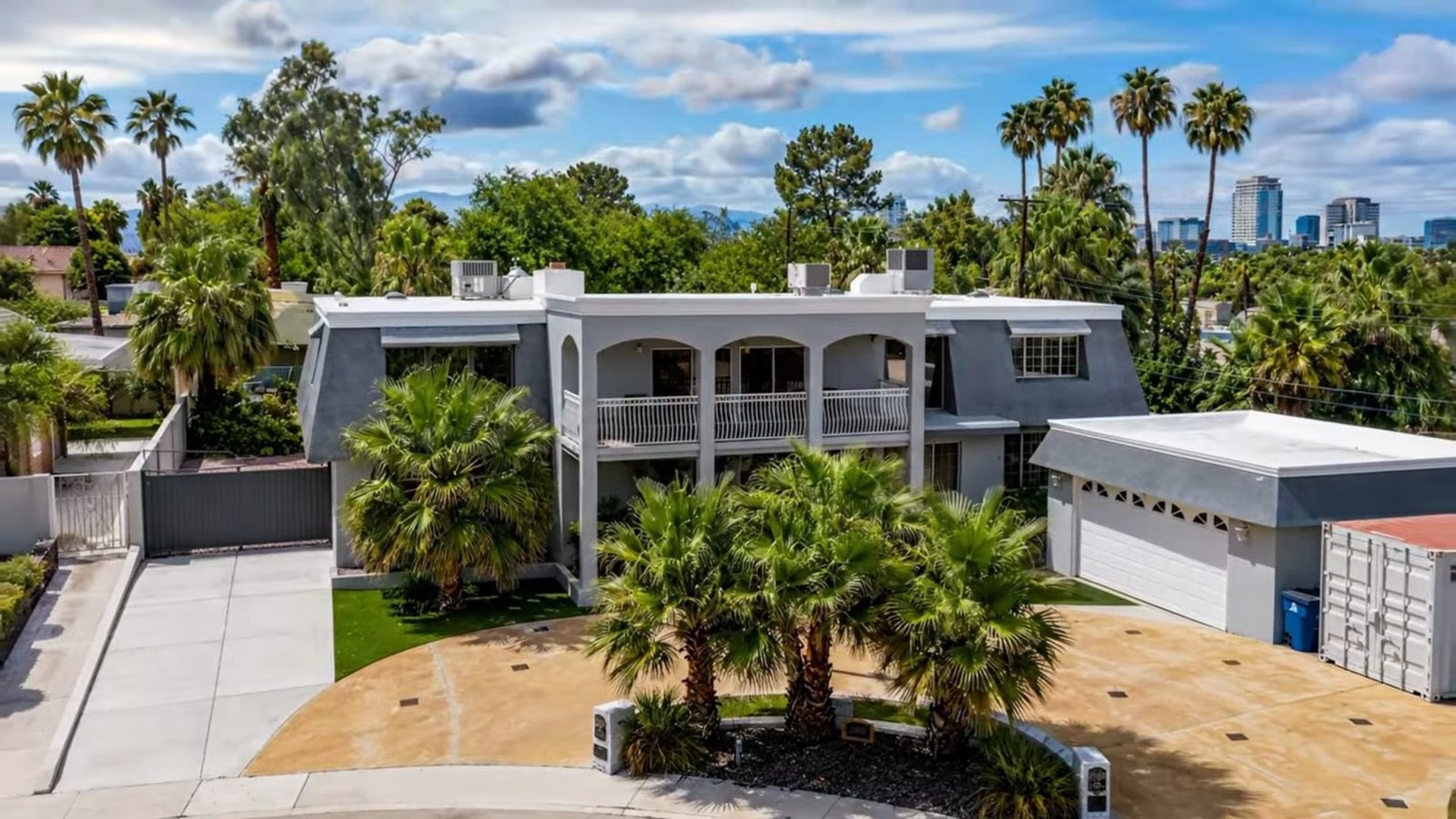 Aerial view of 1400 Maria Elena Drive, a two-story 1970 white stucco estate with arched balconies, palm trees and the downtown Las Vegas skyline behind it