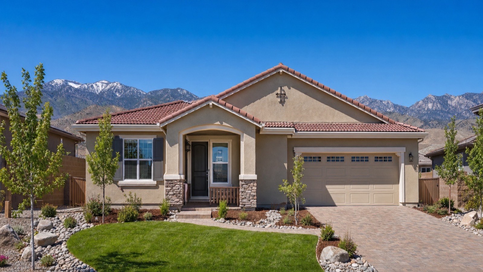 Single-story tan stucco home with a tile roof, two-car garage and front lawn beneath snow-capped mountains