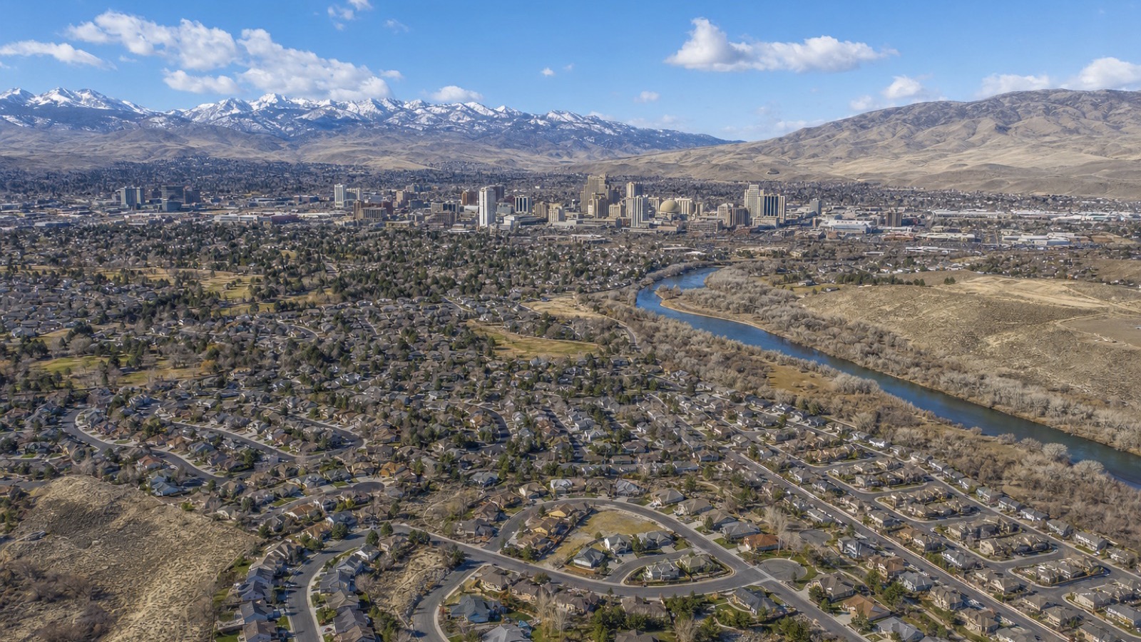 Aerial view of Reno neighborhoods along the Truckee River with downtown and snow-capped Sierra Nevada peaks behind, in Washoe County where the transfer tax is $2.05 per $500
