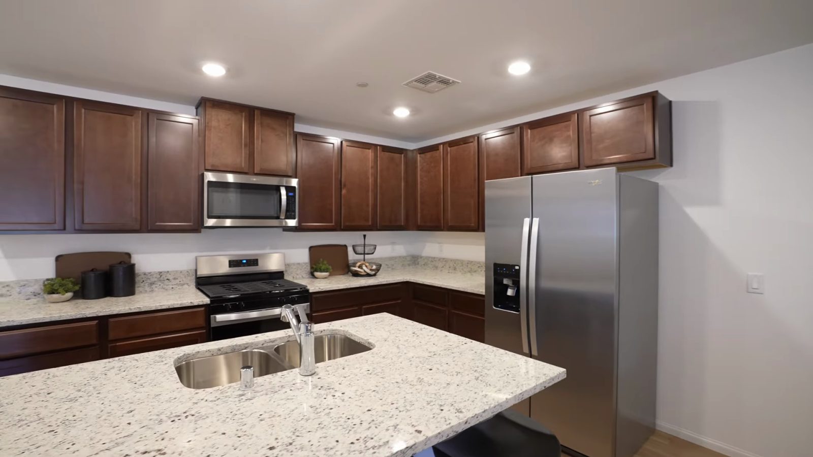 Pulte Cornwall model kitchen at Dalea at Aries with dark stained cabinets, a stone-look island with an undermount sink and stainless appliances