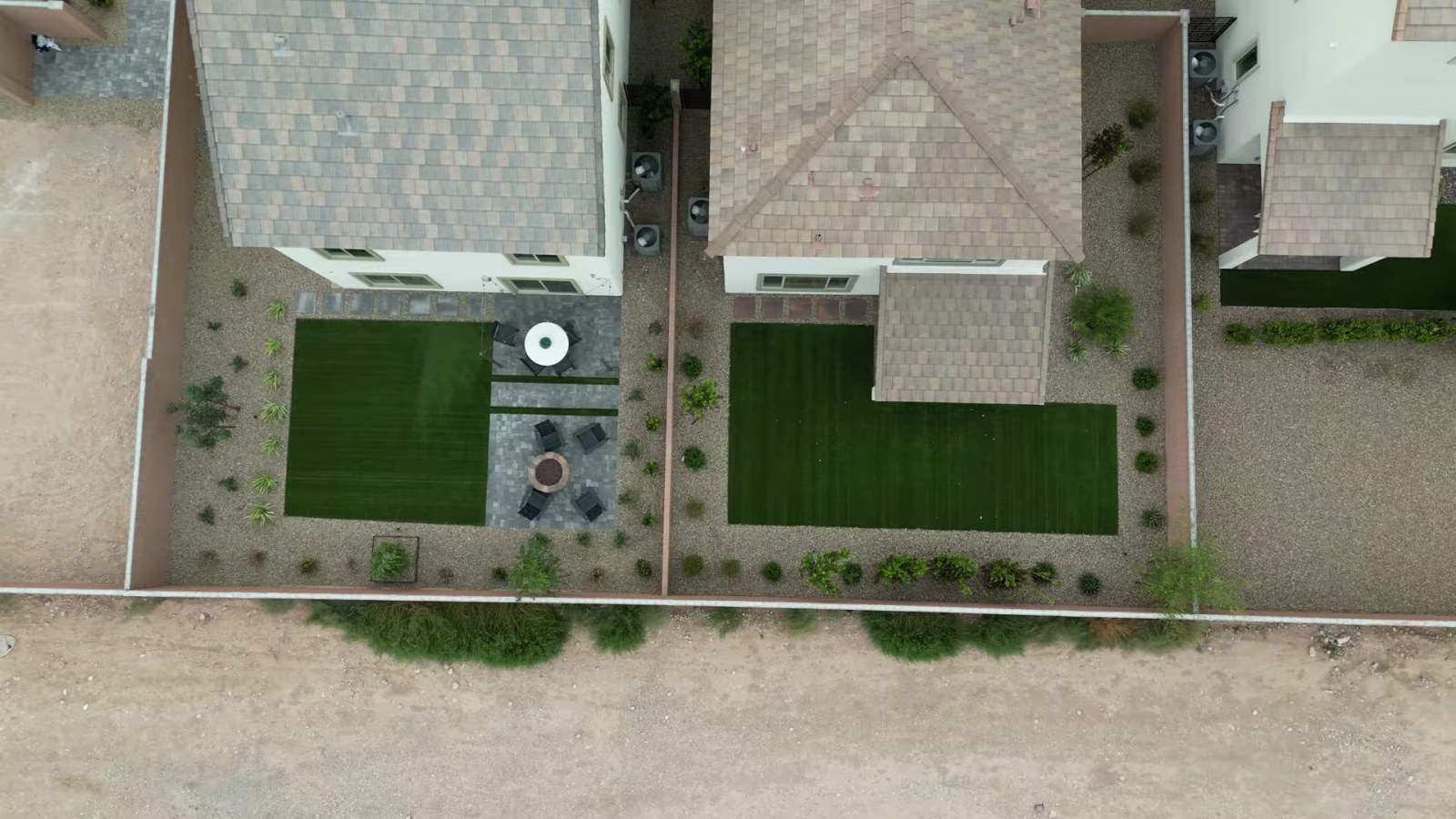 Drone view of two finished model backyards at Cordora with artificial turf, pavers and a covered patio, beside bare unlandscaped ground outside the block walls