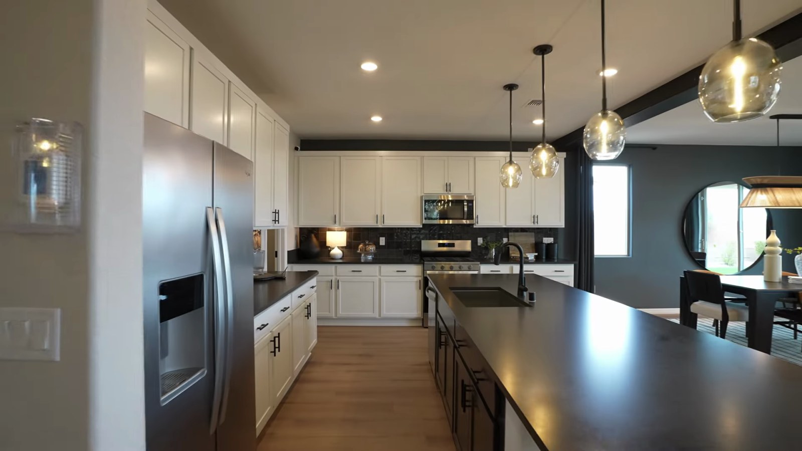 Pulte Juniper model kitchen at Cordora with white cabinets, black countertops, a stainless refrigerator and a long island with seating