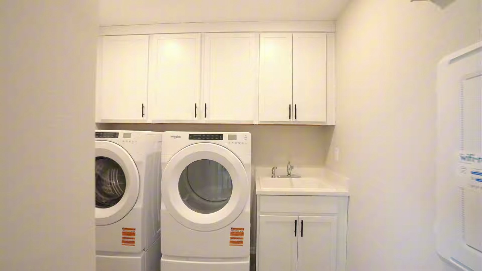 Upstairs laundry room in the Pulte Juniper model with a front-load washer and dryer, a utility sink and white upper and base cabinets