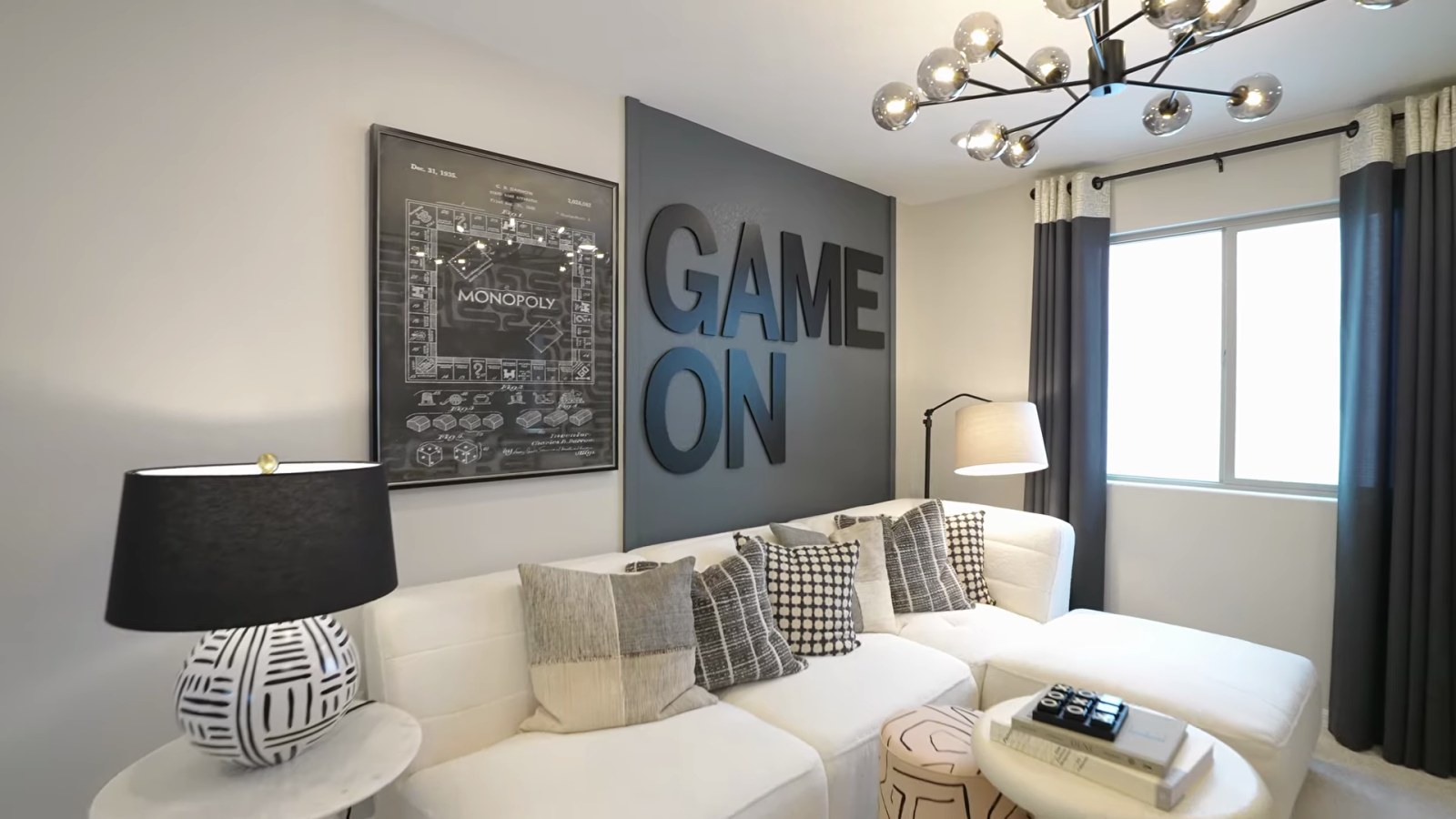 Upstairs loft in the Pulte Juniper model staged as a game room with a white sectional, a modern chandelier and a window
