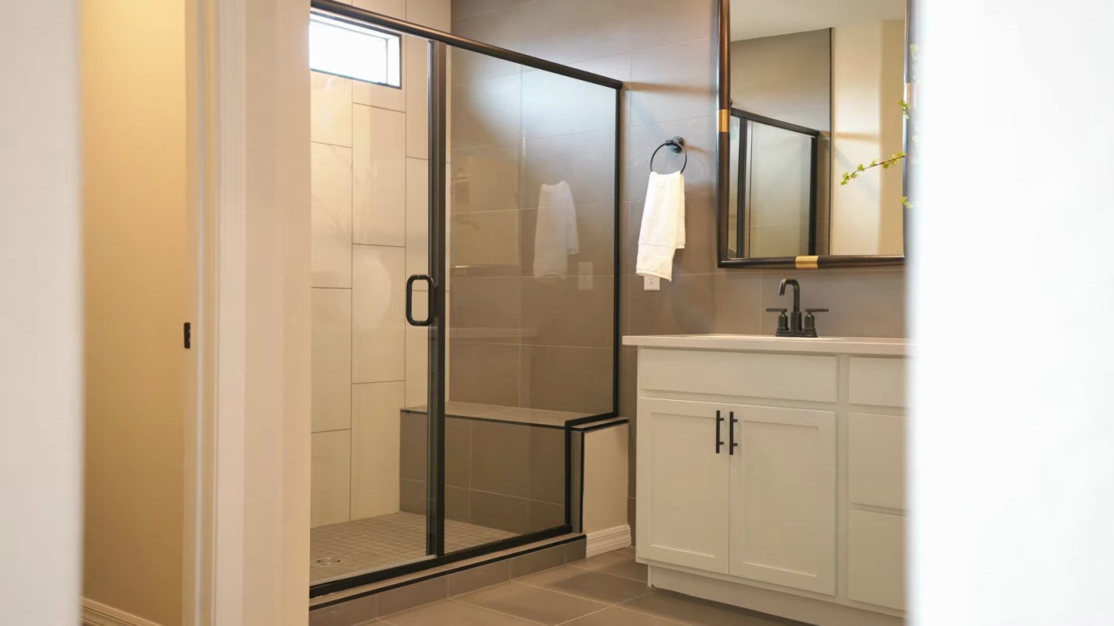 Primary bathroom in the Pulte Juniper model with a glass-enclosed walk-in shower, tall tile walls and a white vanity with a framed mirror