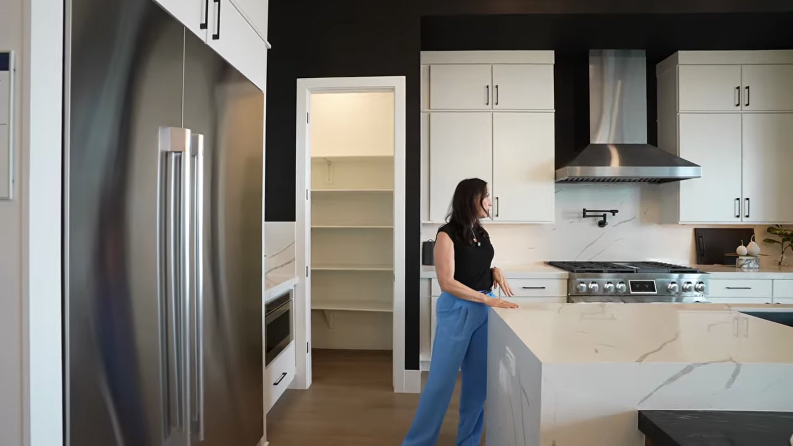 Stacey Tyler in the Pulte Parklane model kitchen at Brantley with white cabinets, a marble-look island, a walk-in pantry and a stainless range hood