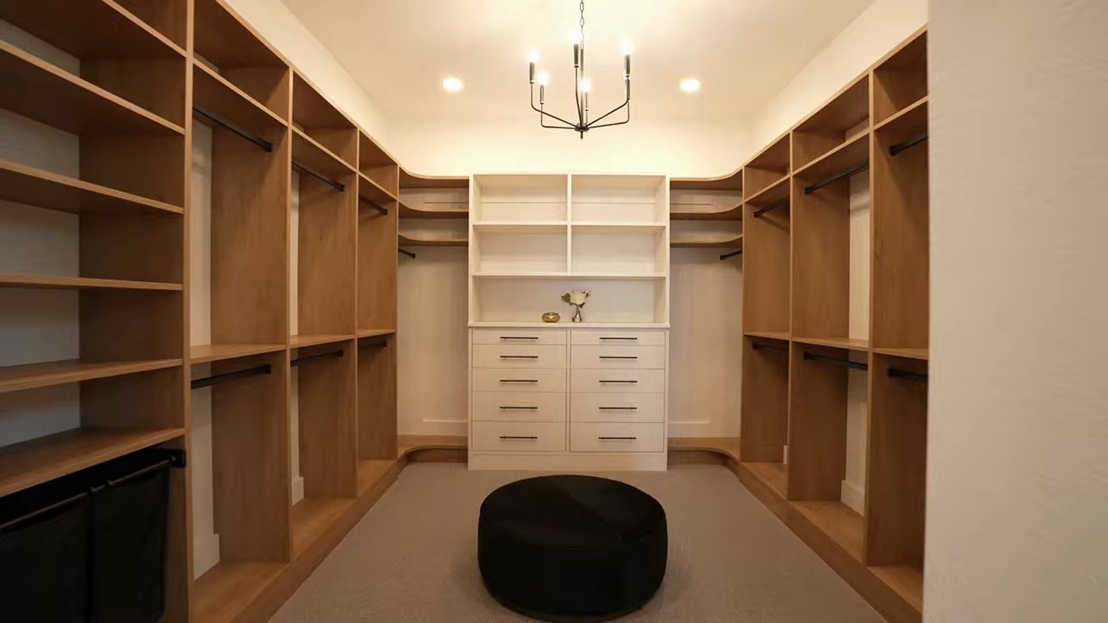 Walk-in primary closet in the Pulte Parklane model at Brantley with wood shelving on three sides, drawers and a center ottoman