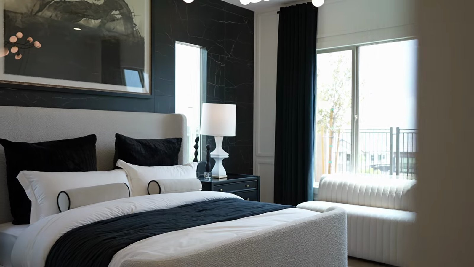 Primary bedroom in the Pulte Parklane model at Brantley with a black stone feature wall, upholstered bed, bench and window to the side yard
