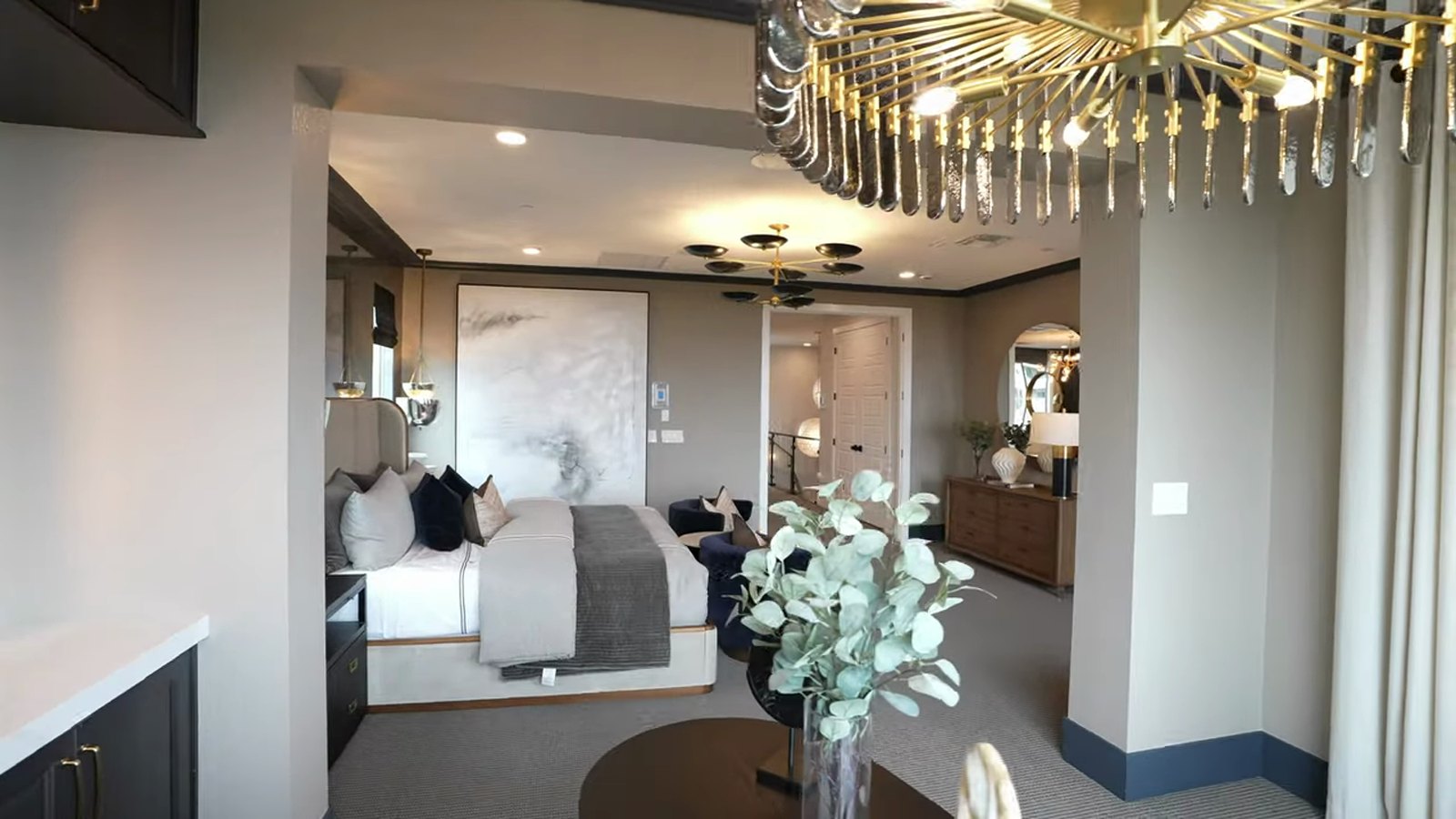 Primary suite in the Pulte Tivoli model at Brantley with a statement chandelier, upholstered bed and owner's retreat beyond