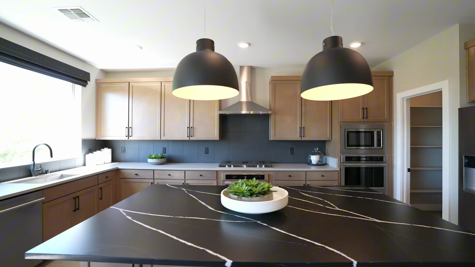 White Pine model kitchen at Delamar with a dark veined quartz island, wood-tone cabinets, a range hood and a stacked wall oven and microwave