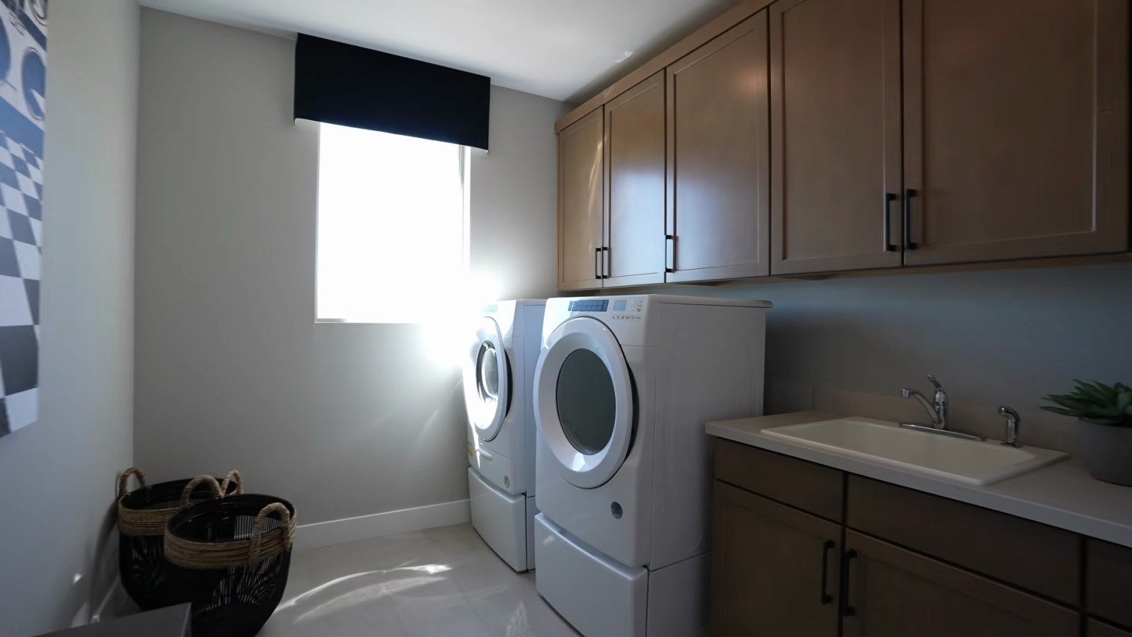 White Pine model laundry room with a front-load washer and dryer on pedestals, upper cabinets and a utility sink beside them