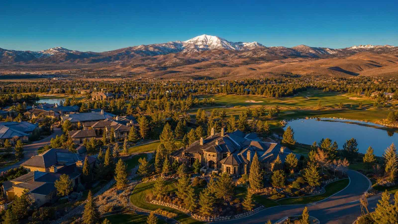 Aerial view of estate homes, pines and a golf course pond in Montreux, south Reno, with snow-capped peaks behind