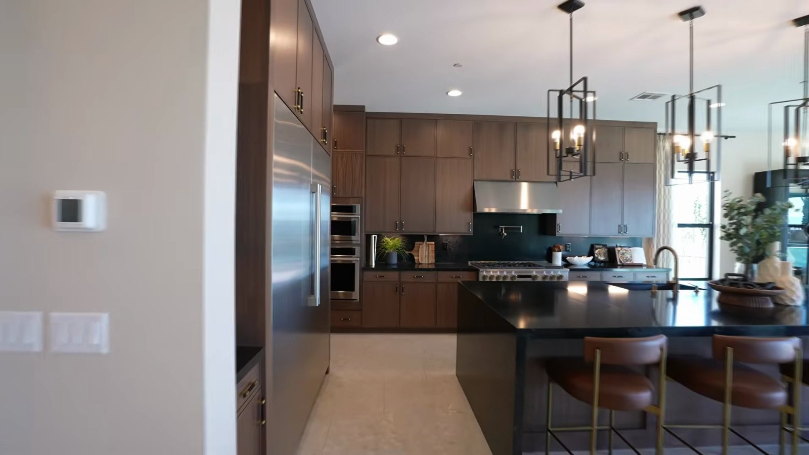 Richmond American Rowan model kitchen with walnut-toned cabinets stacked to the ceiling, a large stainless refrigerator column and an island with bar stools