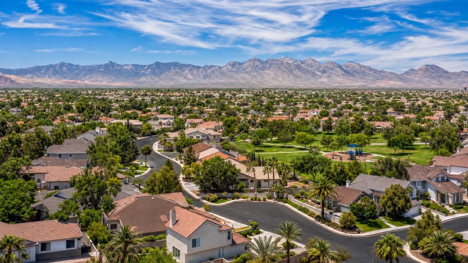 Aerial view of mature Spring Valley streets in Las Vegas with tile-roof resale homes, a park, trees and mountains on the horizon