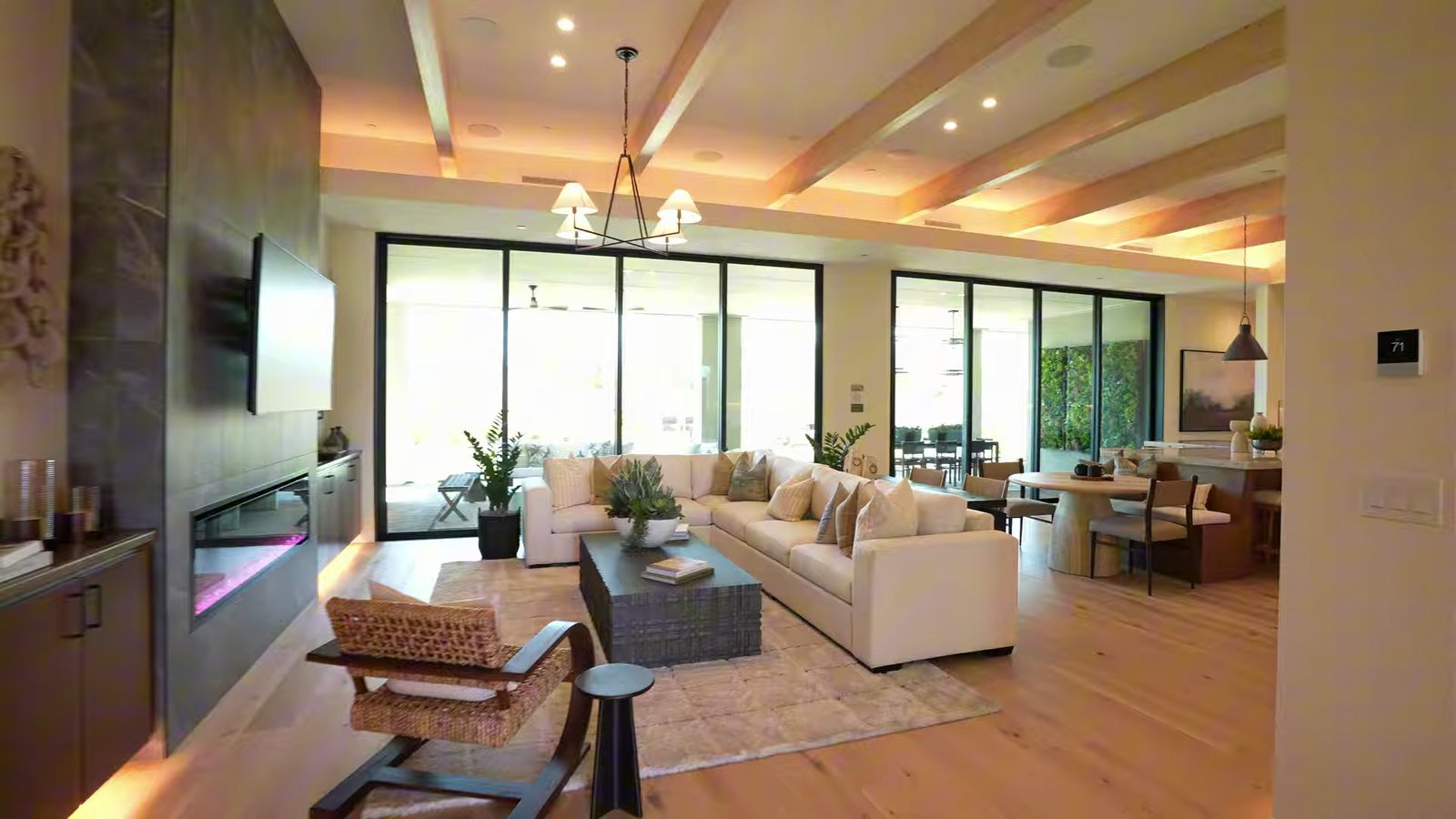 Shawood Kagari great room with exposed wood ceiling beams, a dark stone-look fireplace wall and sliding glass walls to the covered patio