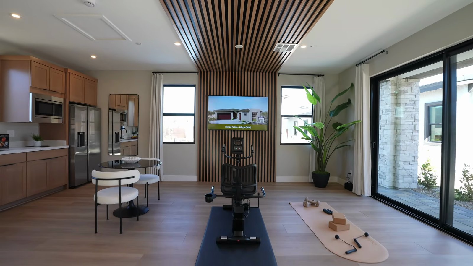 Inside the detached casita at the Quartet model with a wood slat accent wall, an exercise bike, a kitchenette and a sliding glass wall to the patio