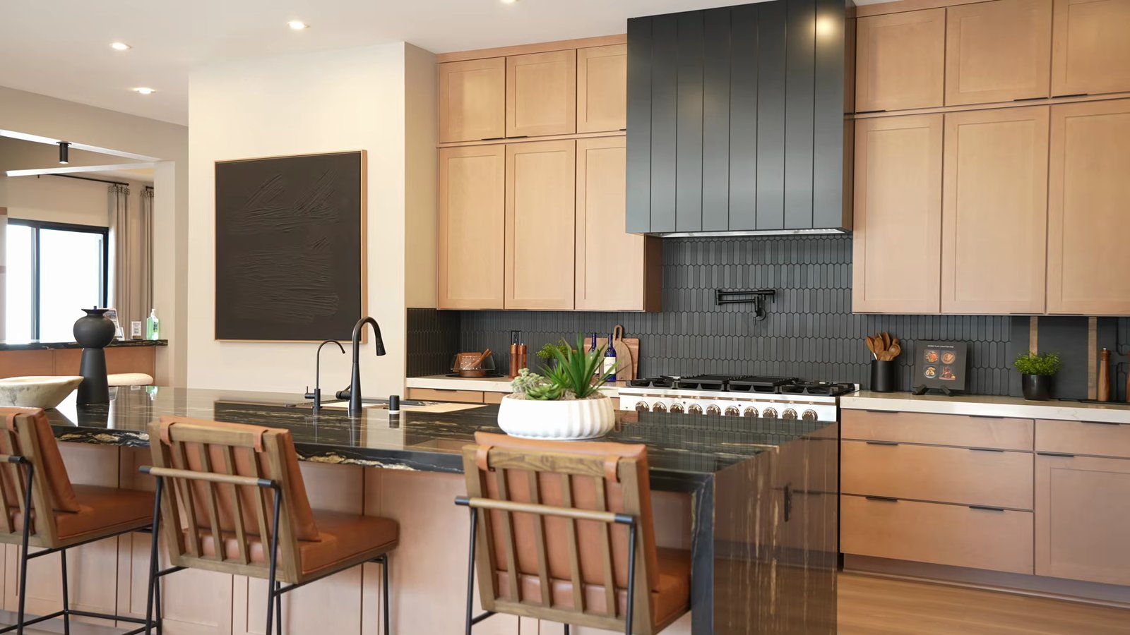 Quartet model kitchen with a dark stone waterfall island, wood cabinets, a 48-inch range under a black hood and bar stools