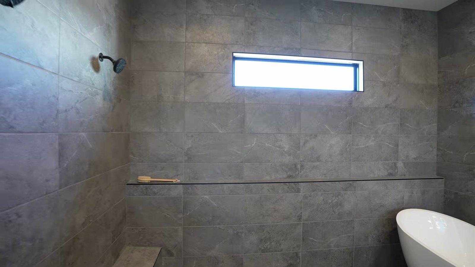 Primary bathroom in the Quartet model with large gray tile, a clerestory window, a wall-mounted shower head and a freestanding tub inside the shower