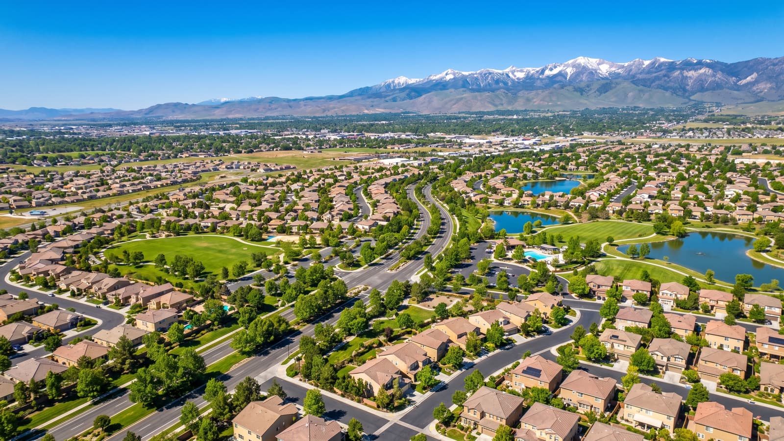 Aerial view of South Reno ZIP 89521 master-planned neighborhoods with green parks and the snow-dusted Sierra Nevada mountains