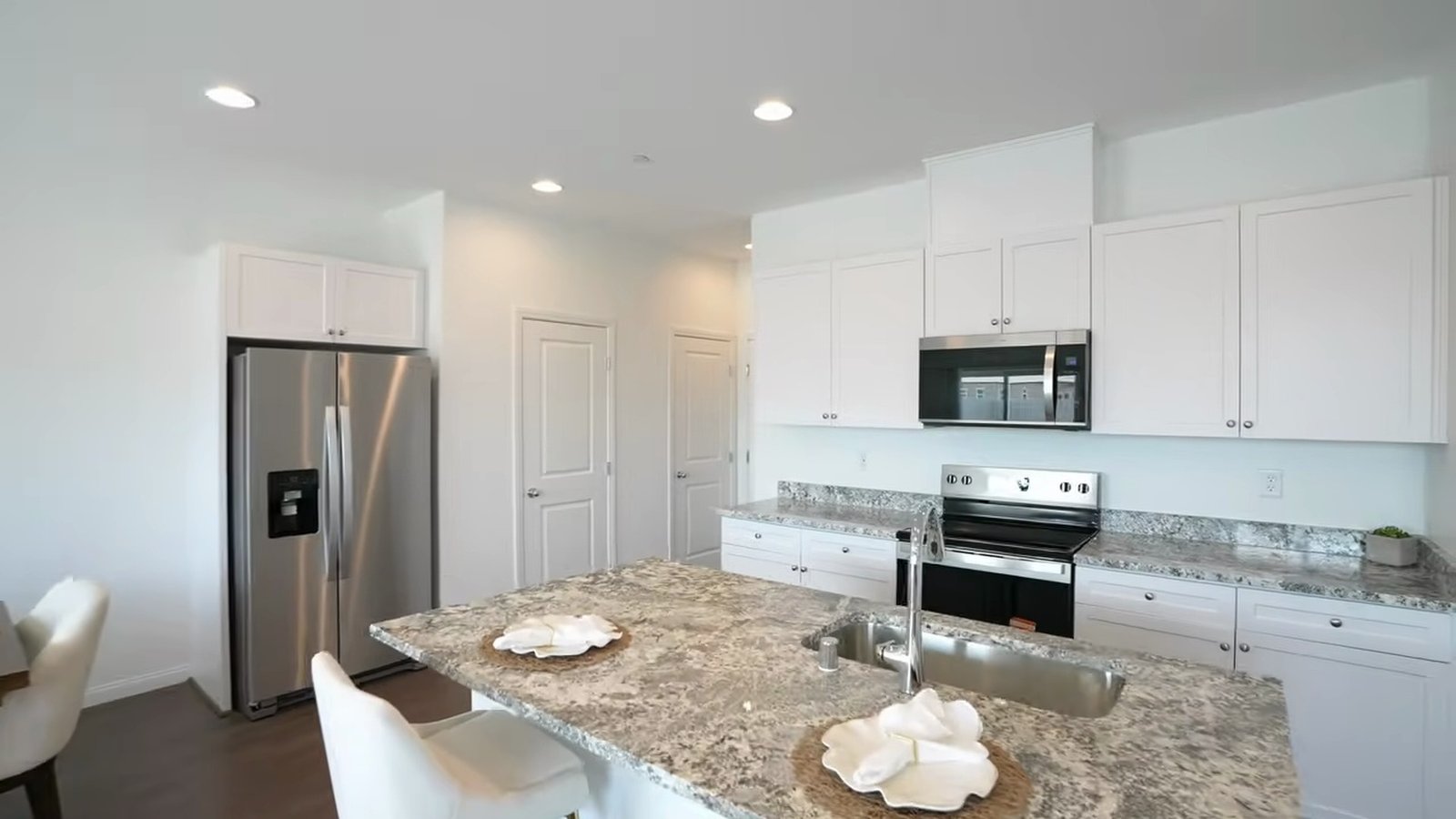 Arroway model kitchen with speckled granite island, undermount sink, white shaker cabinets, stainless refrigerator, range and microwave