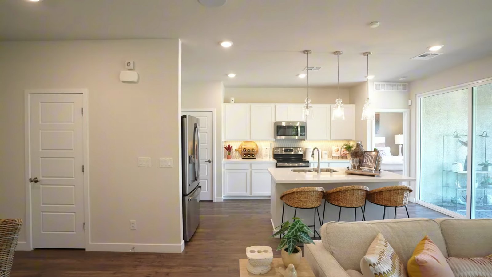 Open great room and kitchen in the Daffodil model at Ovation at Mountain Falls in Pahrump, with a sofa, an island with stools and tall windows to the patio