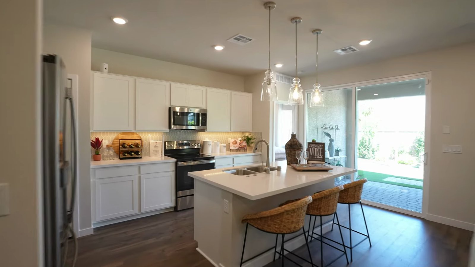 Daffodil model kitchen at Ovation at Mountain Falls with white cabinets, a stainless electric range, an island with pendant lights and a sliding door to the covered patio