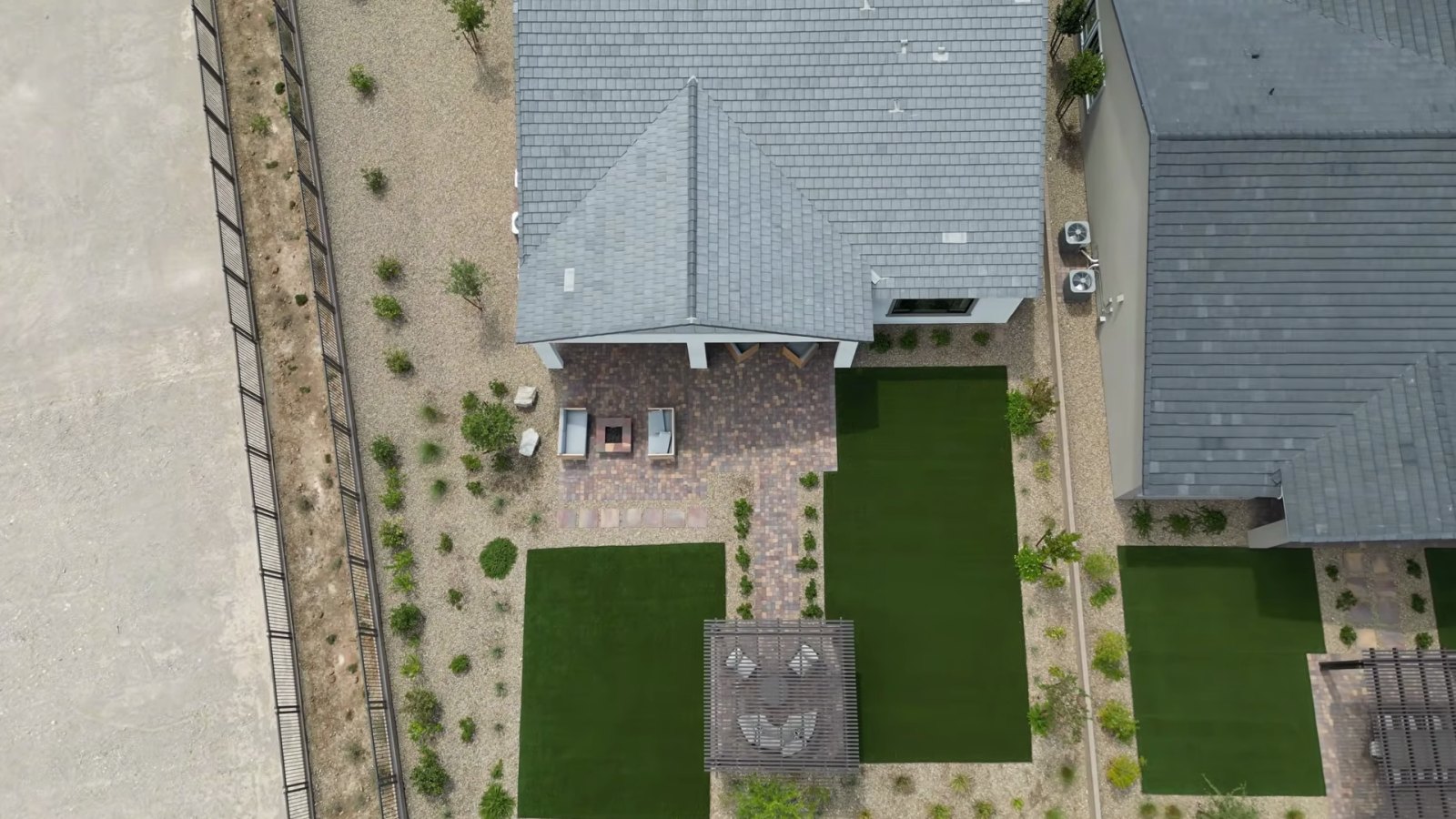 Overhead drone view of the Heritage model backyard at Ashland with a paver patio, fire feature, artificial turf panels and a pergola beside unbuilt land