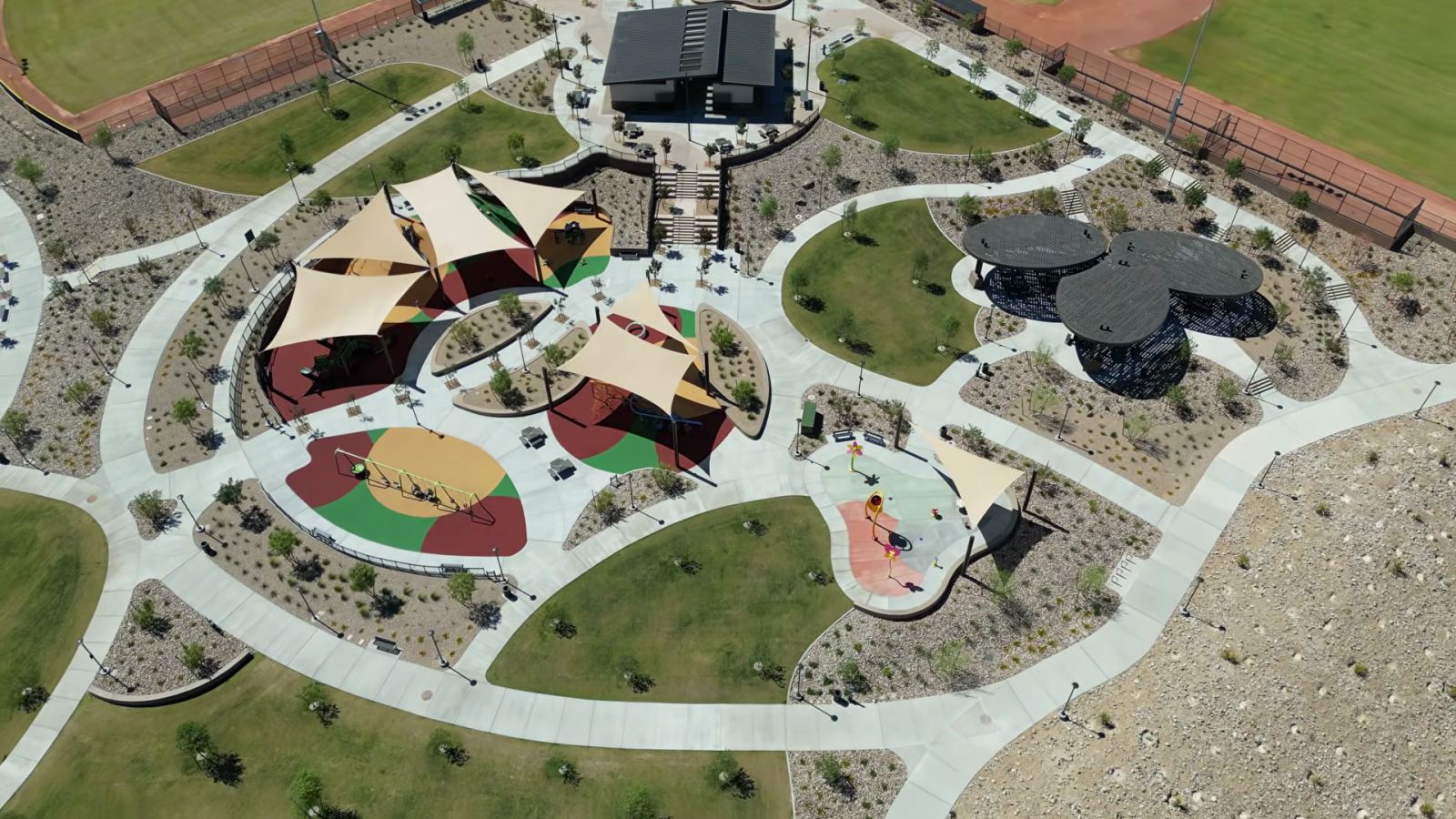 Aerial view of the playground area at Grand Park in Summerlin's Grand Park village, with shade sails, play surfaces, lawns and desert planting