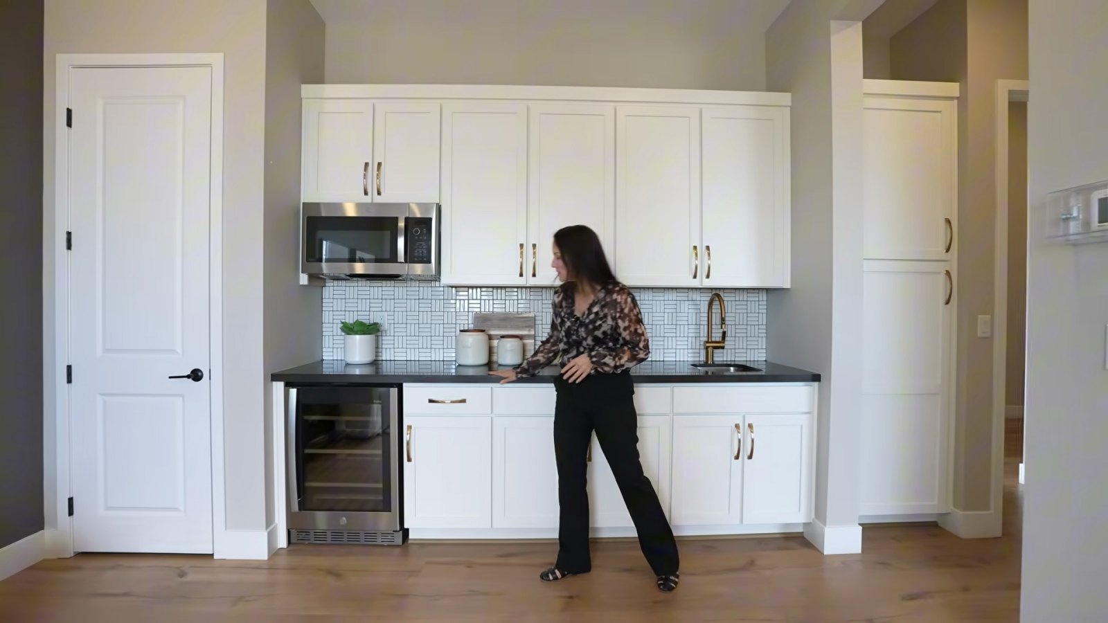 Kitchenette wall in the optional multi-gen suite of the Taylor Morrison Heritage model with white cabinets, a microwave, a beverage refrigerator and a bar sink