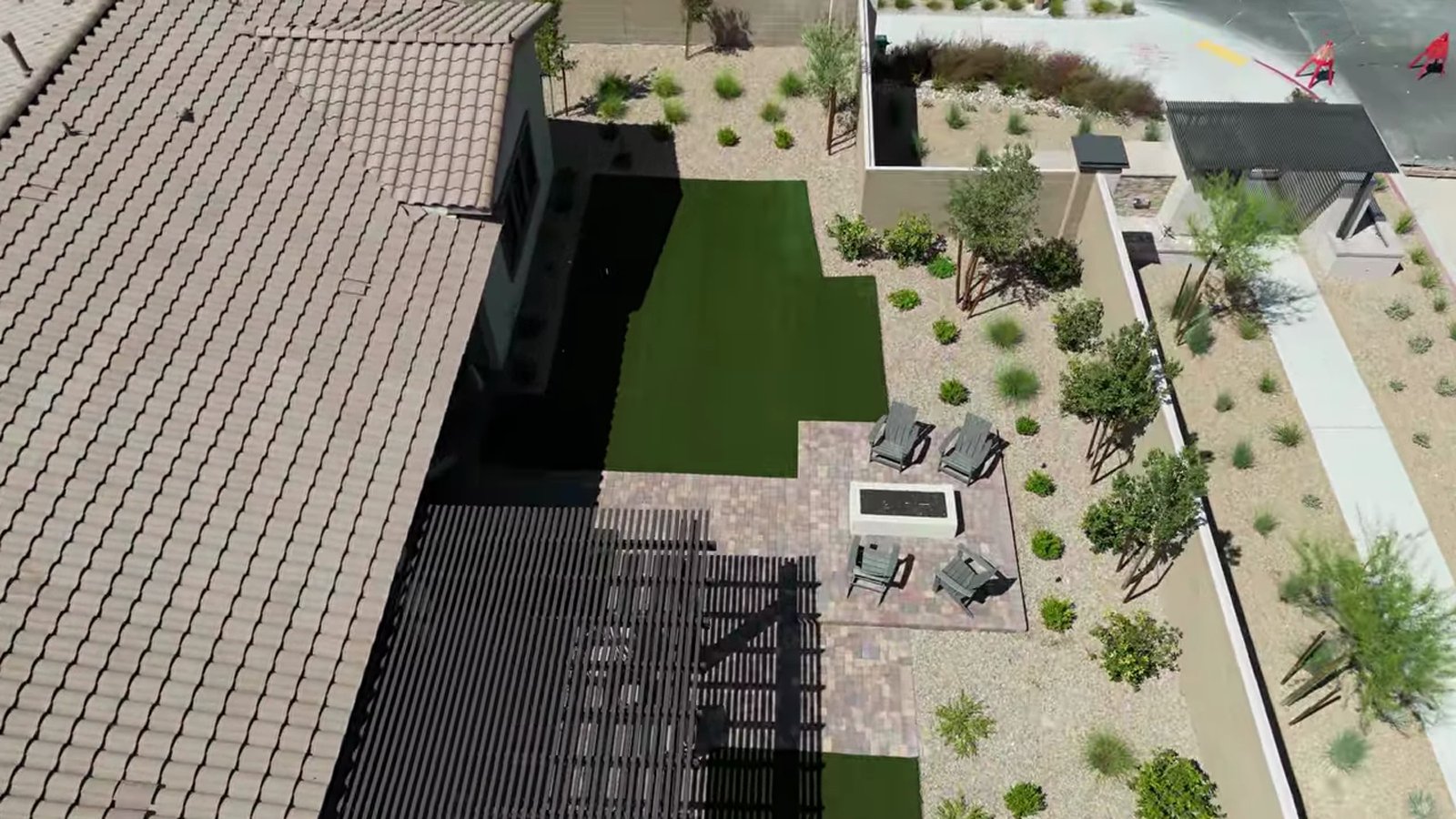 Aerial view of a finished Summit model backyard at Ashland with a pergola, paver patio, fire table, artificial turf and desert planting beside unfinished lots