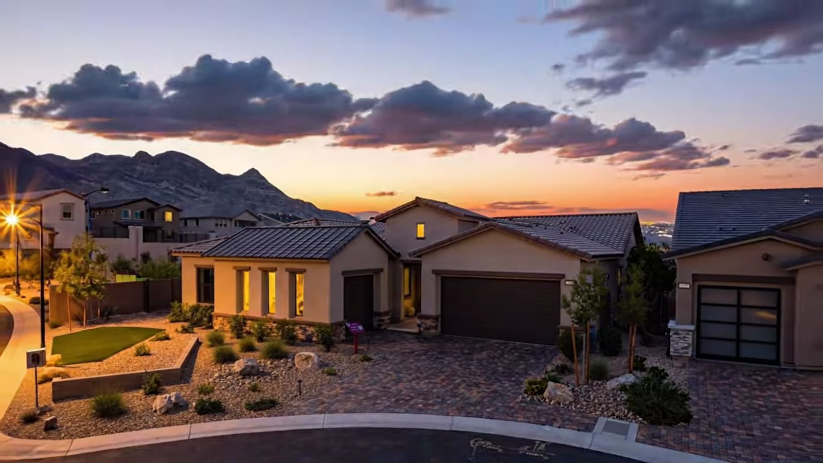 Taylor Morrison Summit model exterior at Ashland in Summerlin at twilight with a three-car garage, desert landscaping and the Spring Mountains behind