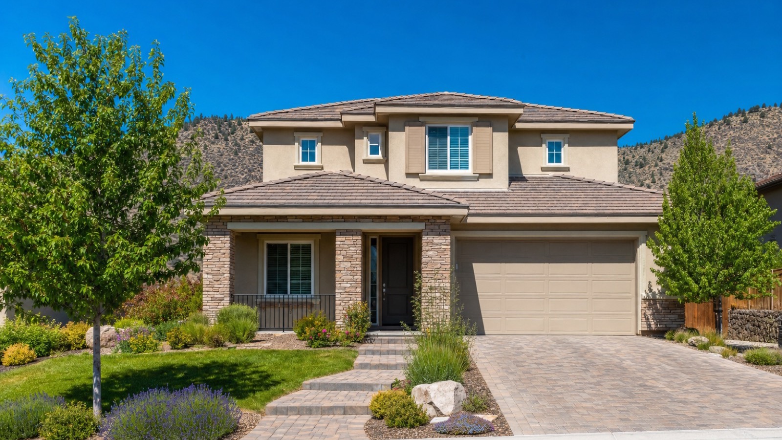 Front exterior of a new two-story Reno home with stone accents, a two-car garage and paver driveway beneath a hillside