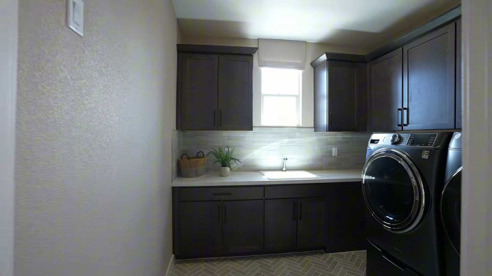 Upstairs laundry room in the Woodside Oakley model at Ashwood with dark cabinets, a utility sink and a front-load washer and dryer