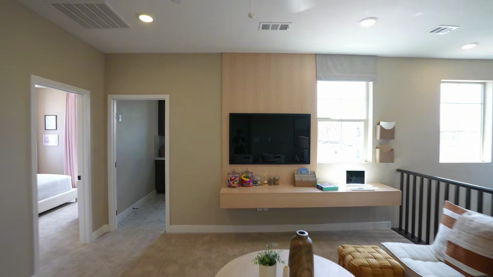 Upstairs loft in the Woodside Oakley model at Ashwood with a television on a wood accent wall, a floating desk and a black stair railing