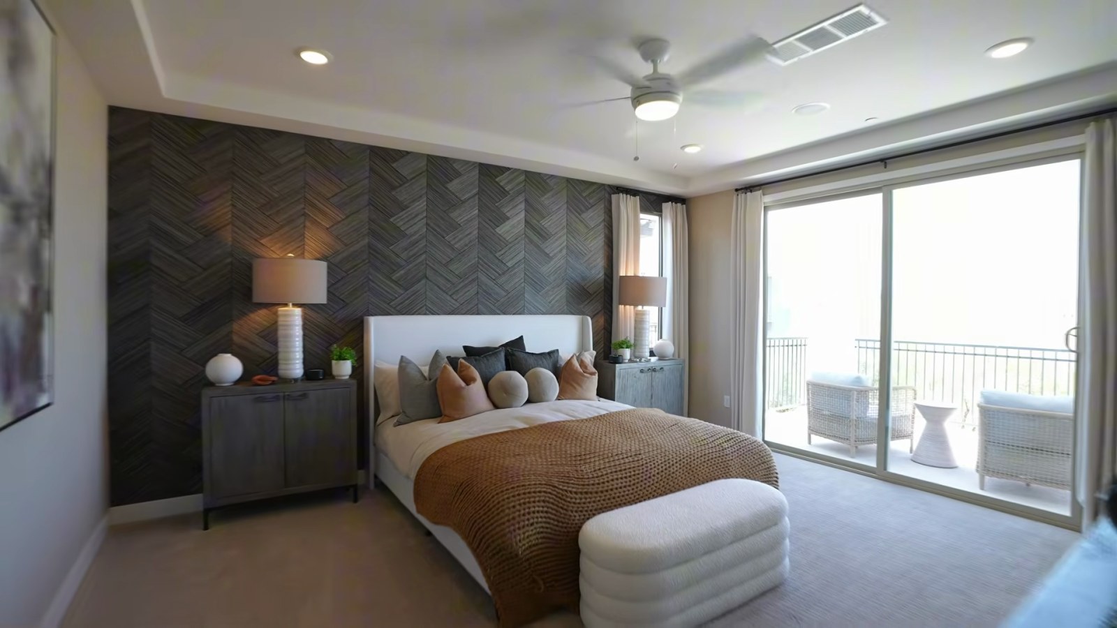 Woodside Oakley primary bedroom at Ashwood with a tray ceiling, a dark chevron accent wall and sliding doors to a balcony