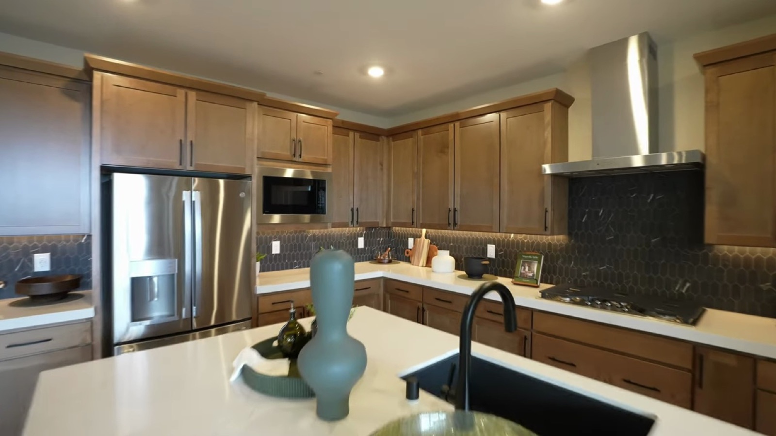 Woodside Oakley model kitchen with wood cabinets, a white quartz island, a dark hexagon tile backsplash and GE stainless appliances